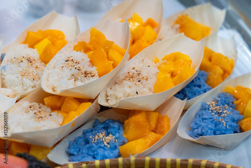 Fototapeta Naklejka Na Ścianę i Meble -  Traditional Thai dessert mango sticky rice served in small leaf-shaped plates with white and blue sticky rice topped with sesame seeds and fresh ripe mango cubes