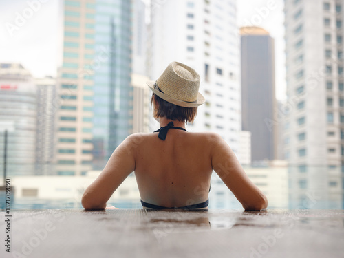 Canvas Print Young asian woman relaxing by pool at Kuala Lumpur hotel with view of surrounding skyscrapers, enjoying leisure time in vibrant urban setting