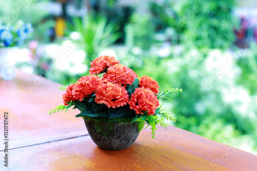 artificial red flowers in decorative flowerpots on brown table wooden. Bouquet of flowers in a pot placed on wooden table with on blurred green background.