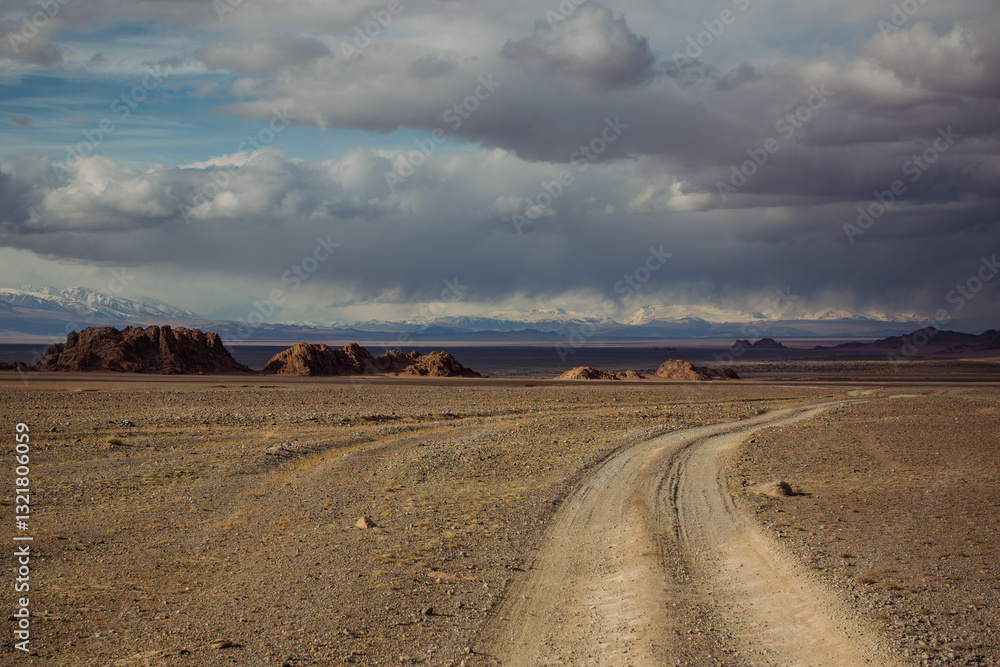 The foothills of western Mongolia with rugged tire tracks etched into the barren landscape, a harsh and untamed beauty.