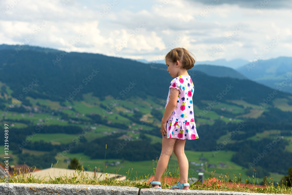 Little girl in colorful dress enjoying scenic mountain view, child walks on a cloudy day