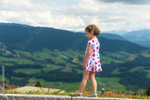 Obraz na płótnie Little girl in colorful dress enjoying scenic mountain view, child walks on a cloudy day w salonie