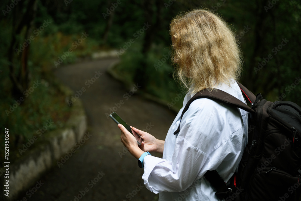Woman with backpack using smartphone on nature trail in forested area