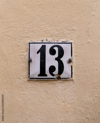 A house number plate with the number 13 on a light-colored wall