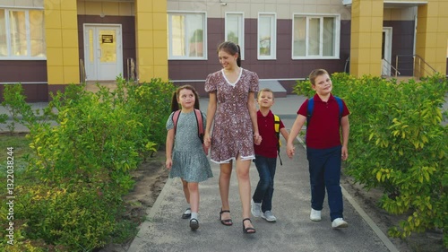 Mother leading children from school, female mother holding children hand, happy family, young nanny with children, schoolchildren with backpacks walking with aunt by the hand, little boys girl walking