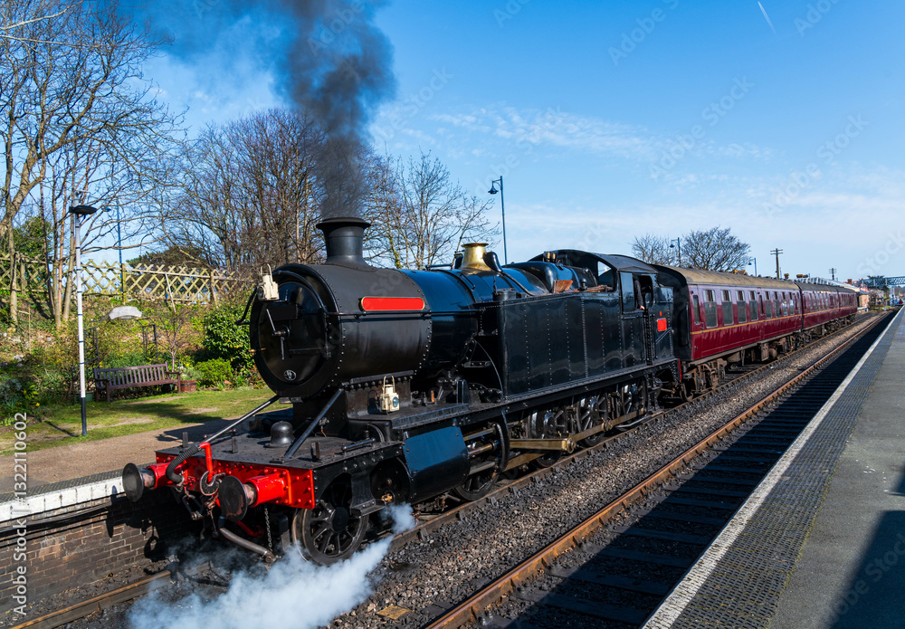 Obraz premium Black Steam Train Engine pulling out of a station, Locomotive pulling carriages exits station, old transportation concept