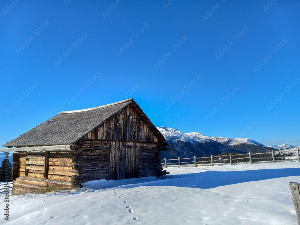 old wooden house in the snowy mountains with a wooden fence and Alps in the background of the ski cabin with a blue sky on a sunny day in the winter