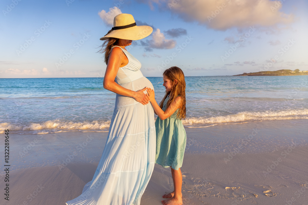A little girl looks at the pregnant belly of her mother in anticipation of her brother or sister on a tropical beach during sunset