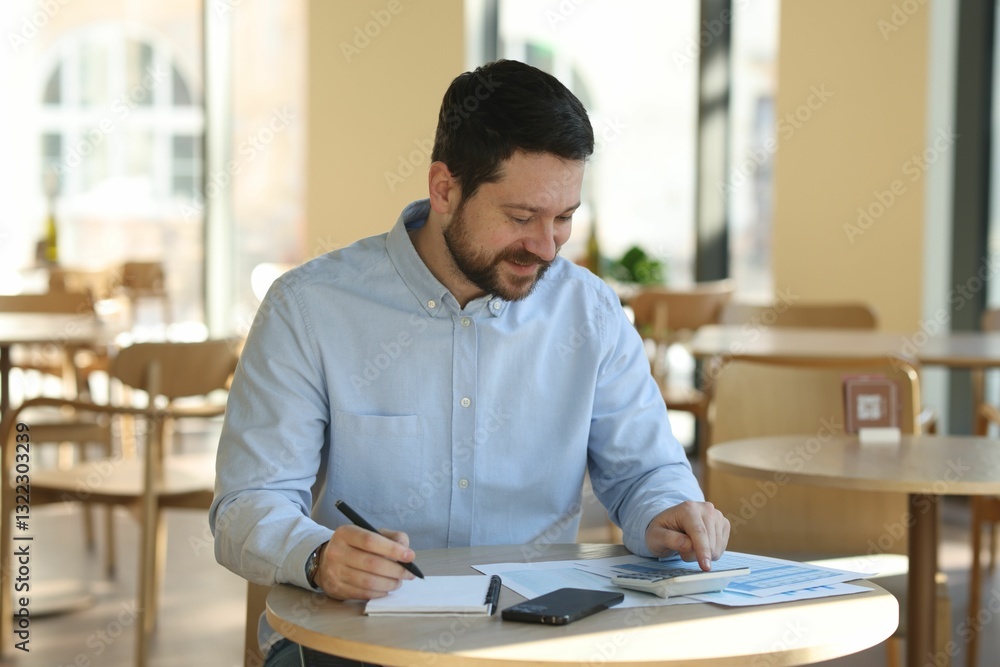 Handsome business owner doing paperwork at table in his cafe Handsome business owner doing paperwork at table in his cafe