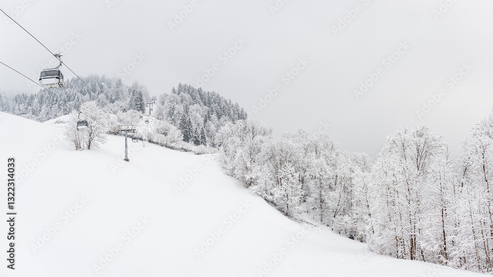 Winter landscape with snowy trees and a gondola railway to the top of the mountain, view during a mountain hike on a hiking trail. Winter day with cloudy and foggy weather.