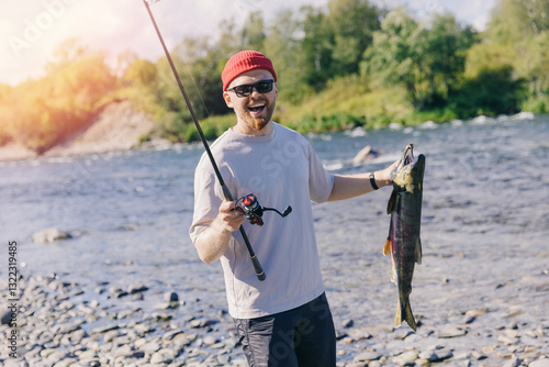 Obraz na plátně Happy man fisherman holding freshly caught salmon fish from mountain river, Kamc