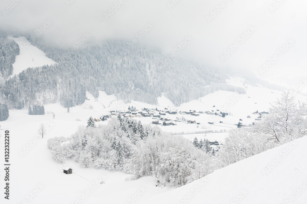 View of a small town in the Alps in a snowy mountain valley. Winter landscape with a view of a mountain hiking trail on a cloudy and foggy day.