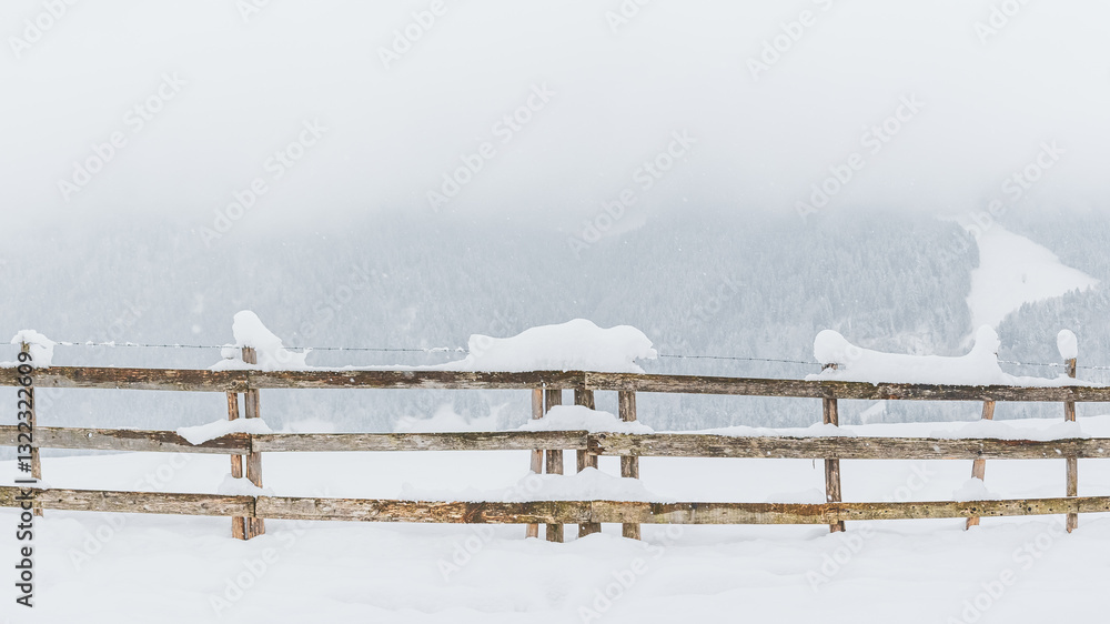 Snow-covered wooden fence on a mountain pasture. Winter landscape on a mountain hiking trail on a cloudy and foggy day.