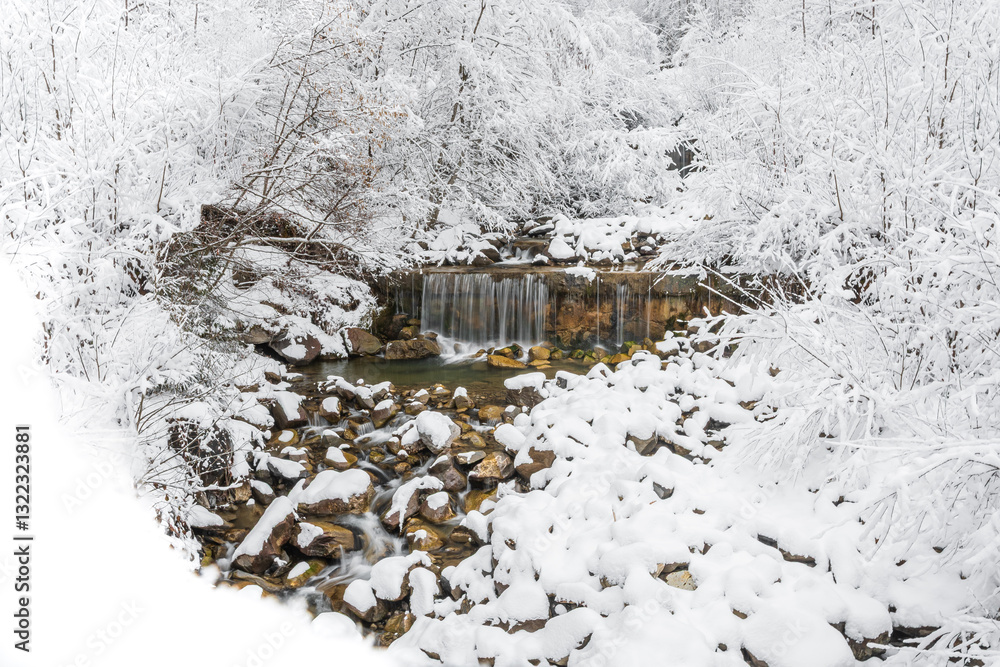 Mountain river in winter, water flows down the riverbed over snow-covered rocks. Winter landscape on a mountain hiking trail.