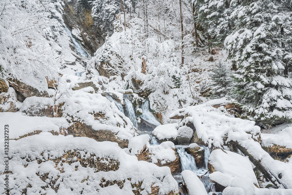 Mountain river in winter, water flows down the riverbed over snow-covered rocks. Winter landscape on a mountain hiking trail.