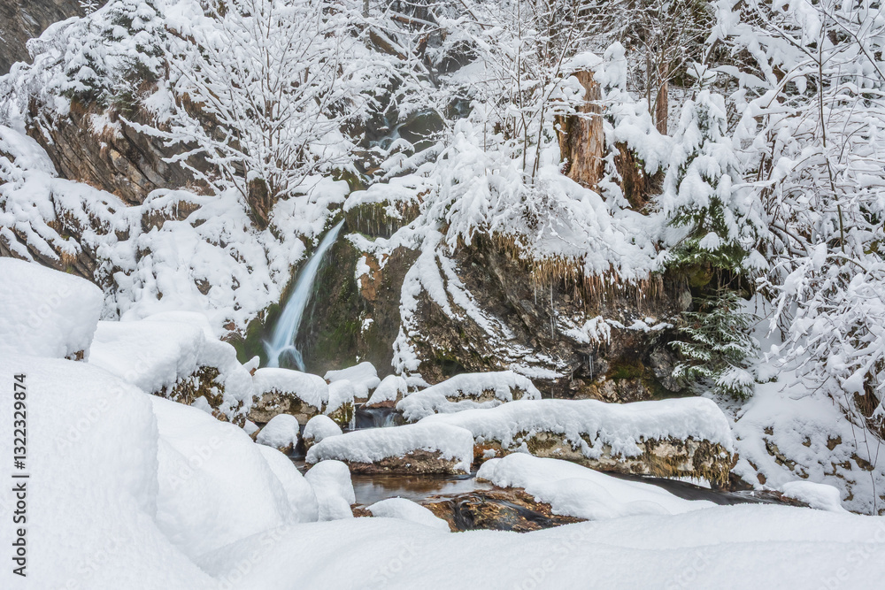 Mountain river in winter, water flows down the riverbed over snow-covered rocks. Winter landscape on a mountain hiking trail.