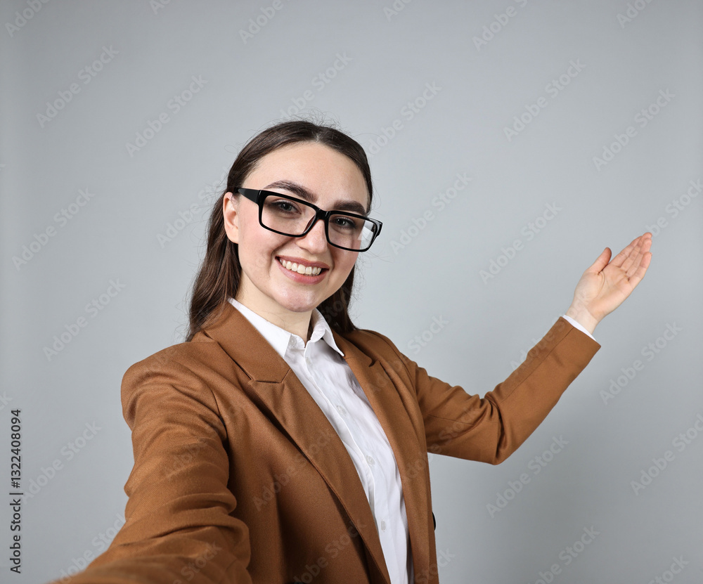 Happy businesswoman welcoming clients or partners by video call on grey background, view through camera Happy businesswoman welcoming clients or partners by video call on grey background, view through camera