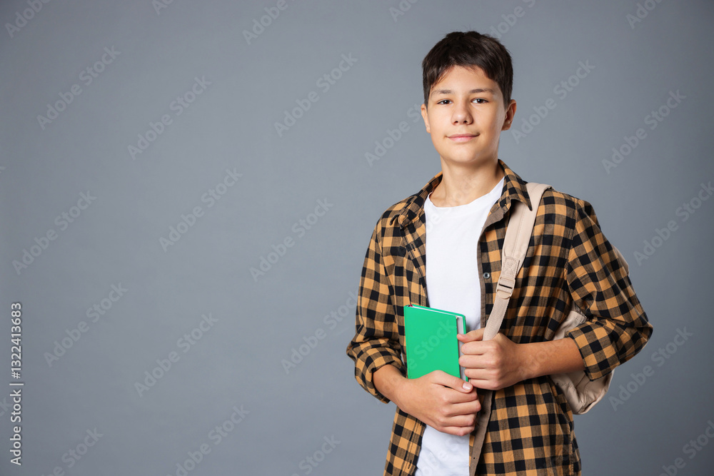 Portrait of teenage boy with book and backpack on grey background, space for text Portrait of teenage boy with book and backpack on grey background, space for text