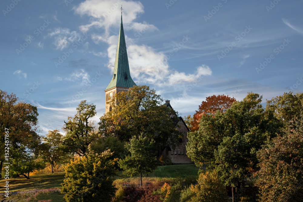 Fototapeta premium Stone church surrounded by trees against blue cloudy sky on an autumn day