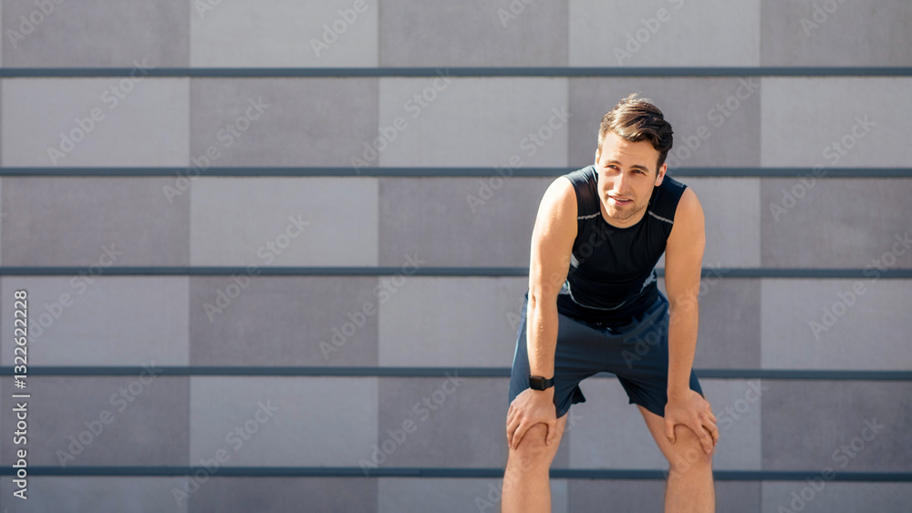 Fototapeta premium Respite in training. Tired handsome man in sportswear with smart watch stopped at workout on gray wall background, free space