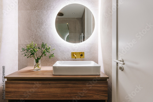 A modern bathroom with a round, backlit mirror above a wooden vanity photo