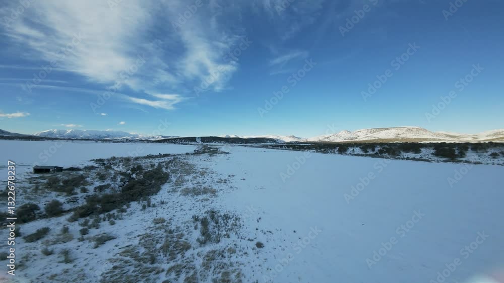 Aerial-FPV-First person view - Flying over snow covered field in shade of sun gone down behind the west mountain with sunlight still hitting distant hills Aerial-FPV-First person view - Flying over snow covered field in shade of sun gone down behind the west mountain with sunlight still hitting distant hills