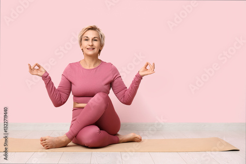 Portrait of meditating mature woman sitting on floor against pink wall