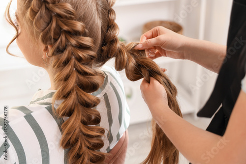 Фотография Professional hairdresser braiding client's hair in salon, closeup