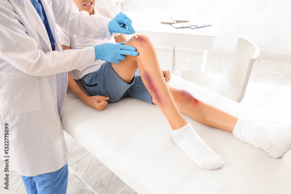 Naklejka premium Female doctor treating little boy's wounded leg in clinic, closeup