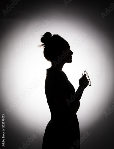 black and white silhouette profile of a woman with her hair in a bun holding reading glasses