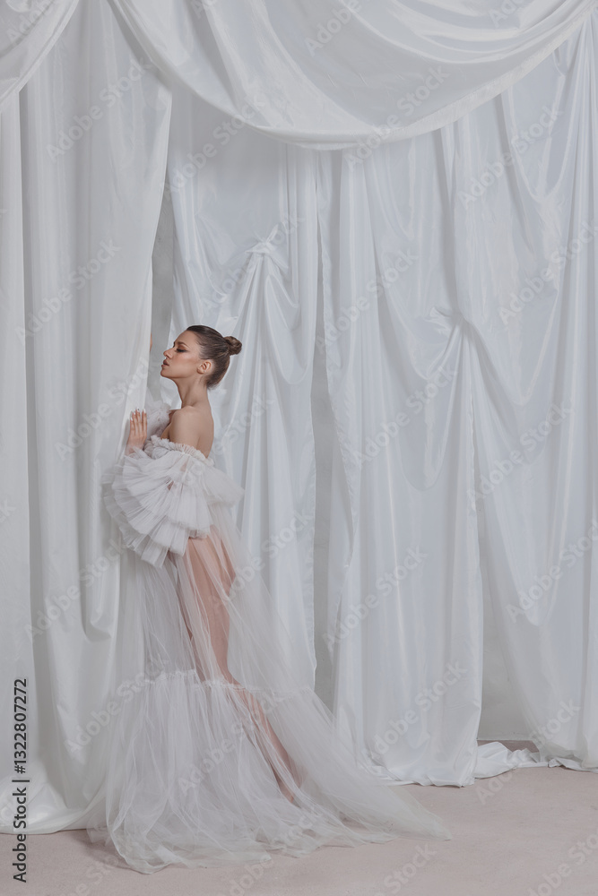 Model stands gracefully in a stunning white gown, leaning against a soft draped fabric backdrop. setting highlights the delicate fabric and the models elegant pose during a fashion shoot Model stands gracefully in a stunning white gown, leaning against a soft draped fabric backdrop. setting highlights the delicate fabric and the models elegant pose during a fashion shoot
