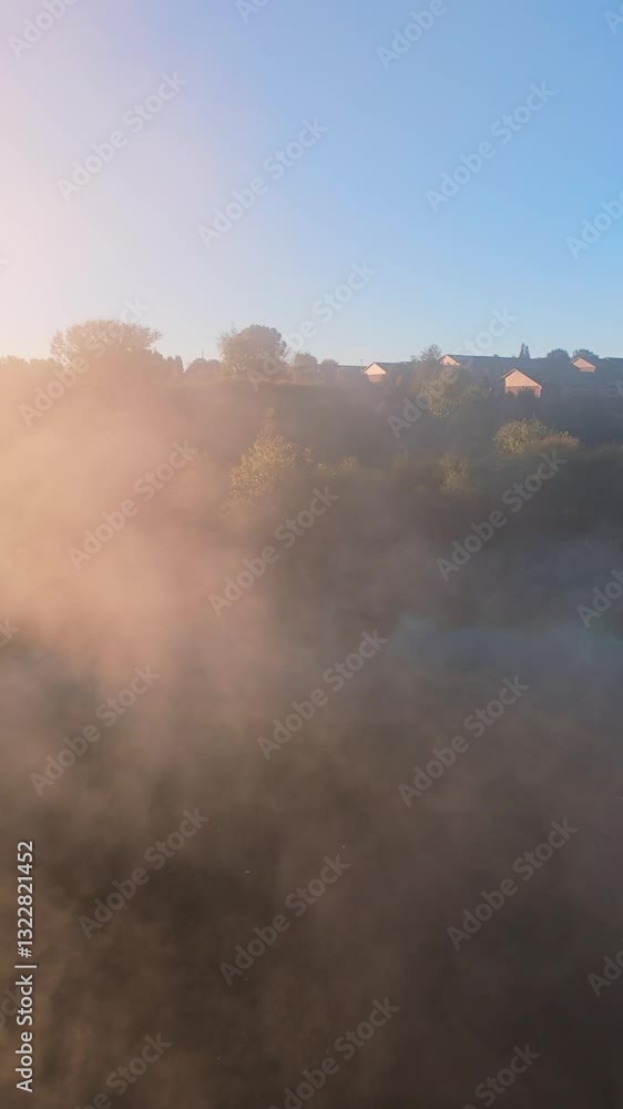 Vertical screen Misty Landscape at Sunrise with Sunlight Glow scenic misty landscape at sunrise, with golden sunlight illuminating fog and distant houses on hill under clear blue sky. Vertical screen Misty Landscape at Sunrise with Sunlight Glow scenic misty landscape at sunrise, with golden sunlight illuminating fog and distant houses on hill under clear blue sky.