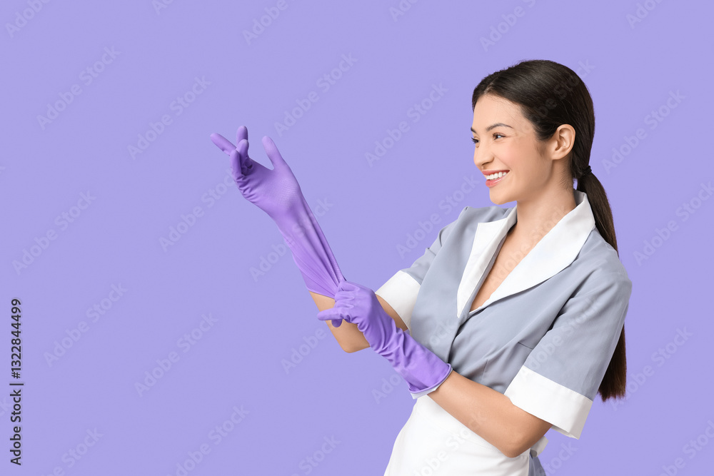 Beautiful young chambermaid putting on rubber gloves on purple background Beautiful young chambermaid putting on rubber gloves on purple background