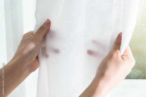 Close-up of woman hand opening white fabric curtain at home.