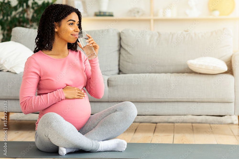 Young black pregnant woman drinking water after training at home, looking at copy space Young black pregnant woman drinking water after training at home, looking at copy space