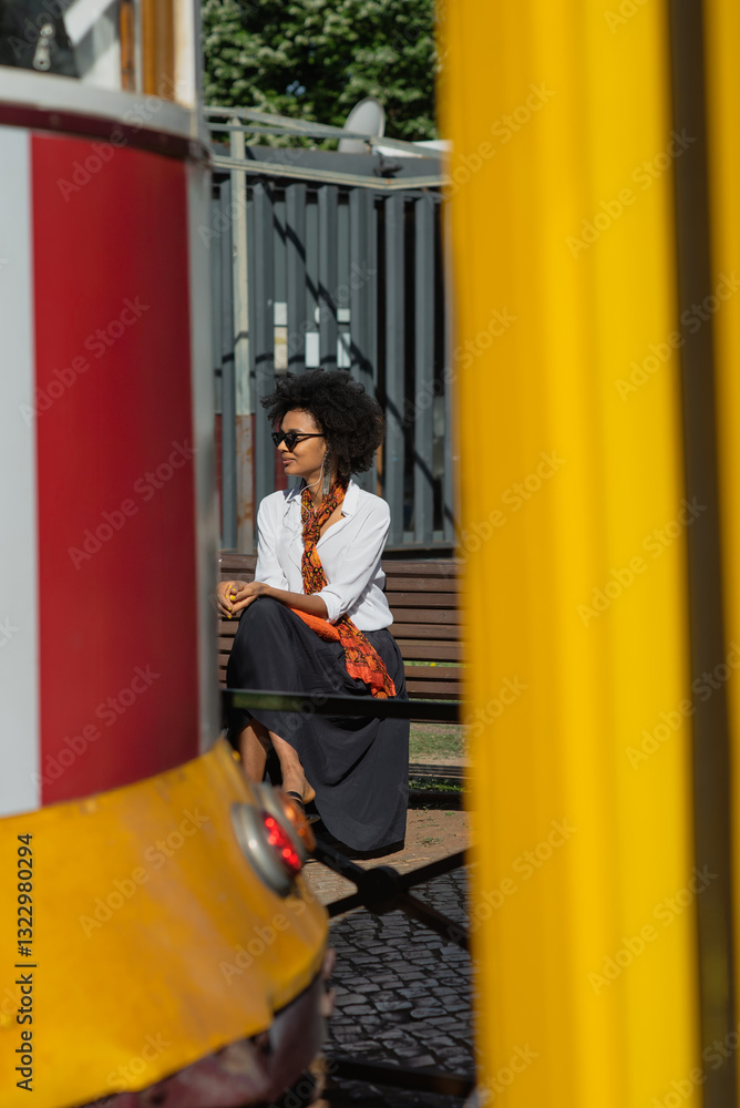 © tessy morelli/Stocksy - Woman sitting on bench waiting for tram 28 in Lisbon © tessy morelli/Stocksy - Woman sitting on bench waiting for tram 28 in Lisbon
