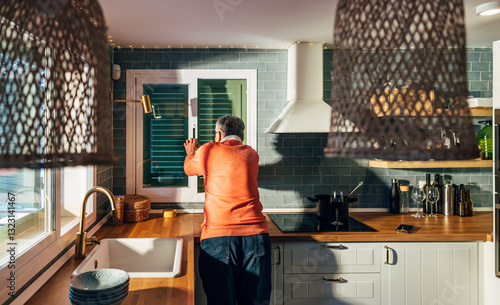 Man in cozy kitchen looking out window at morning light photo