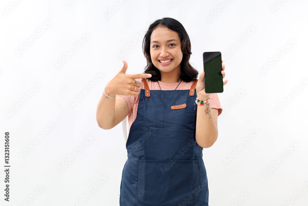 Beautiful asian barista in blue apron pointing finger at mobile screen, showing app and smiling, standing over white background Beautiful asian barista in blue apron pointing finger at mobile screen, showing app and smiling, standing over white background