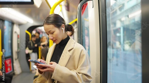 Asian businesswoman using mobile phone online working corporate business chatting with AI on train. Happy woman listening to music on earphones and using smartphone during travel in the city on tram.