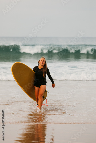 A smiling female surfer walks back from the ocean carrying her b photo