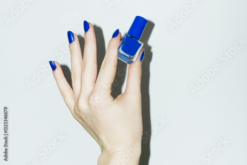 Hand with royal blue manicure holding beauty product nail polish