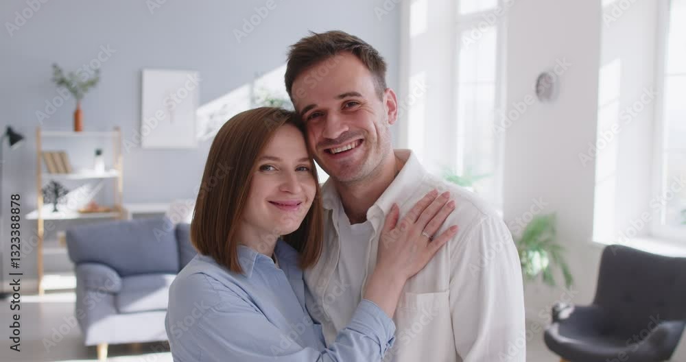 Smiling couple at home, family portrait of happy husband, wife standing close hugging, looking at camera posing, lovers embrace showing love, care affection, relaxing weekend together in modern flat Smiling couple at home, family portrait of happy husband, wife standing close hugging, looking at camera posing, lovers embrace showing love, care affection, relaxing weekend together in modern flat