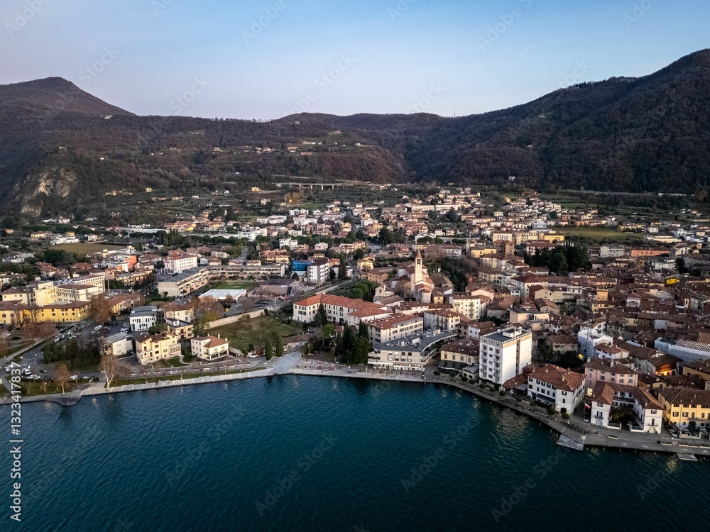 View of a picturesque Italian town by a lake surrounded by hills at sunset in Iseo View of a picturesque Italian town by a lake surrounded by hills at sunset in Iseo