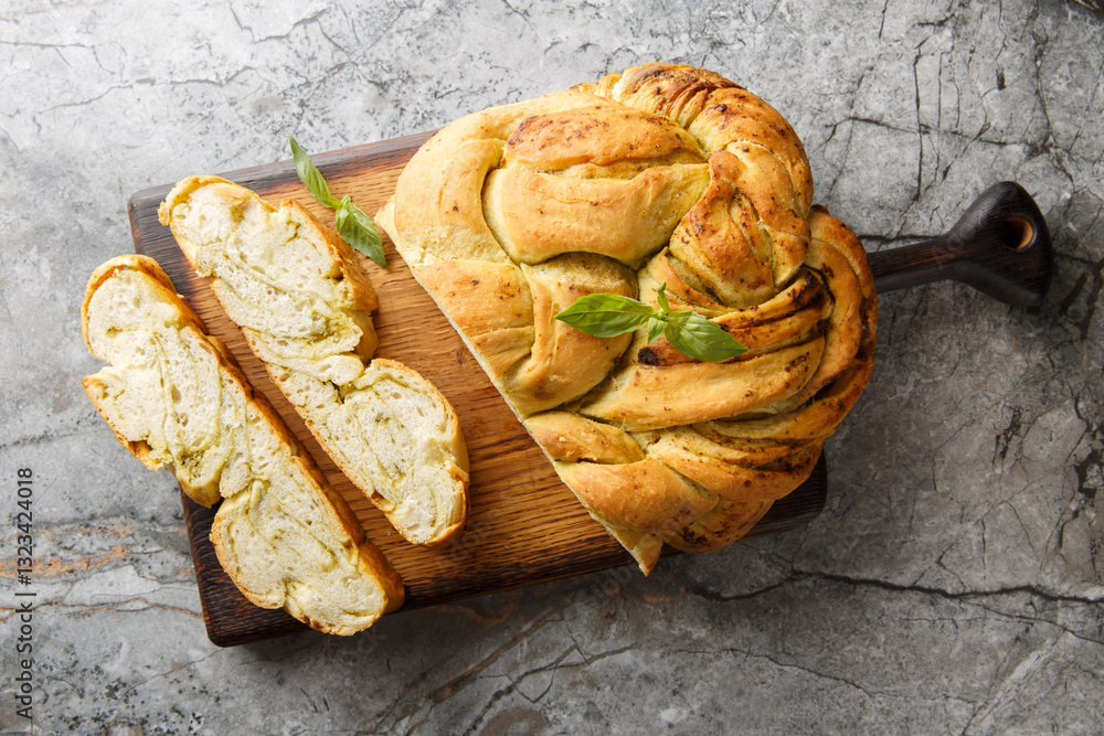 Fresh basil pesto braided bread close-up on wooden board on table. Horizontal top view from above
