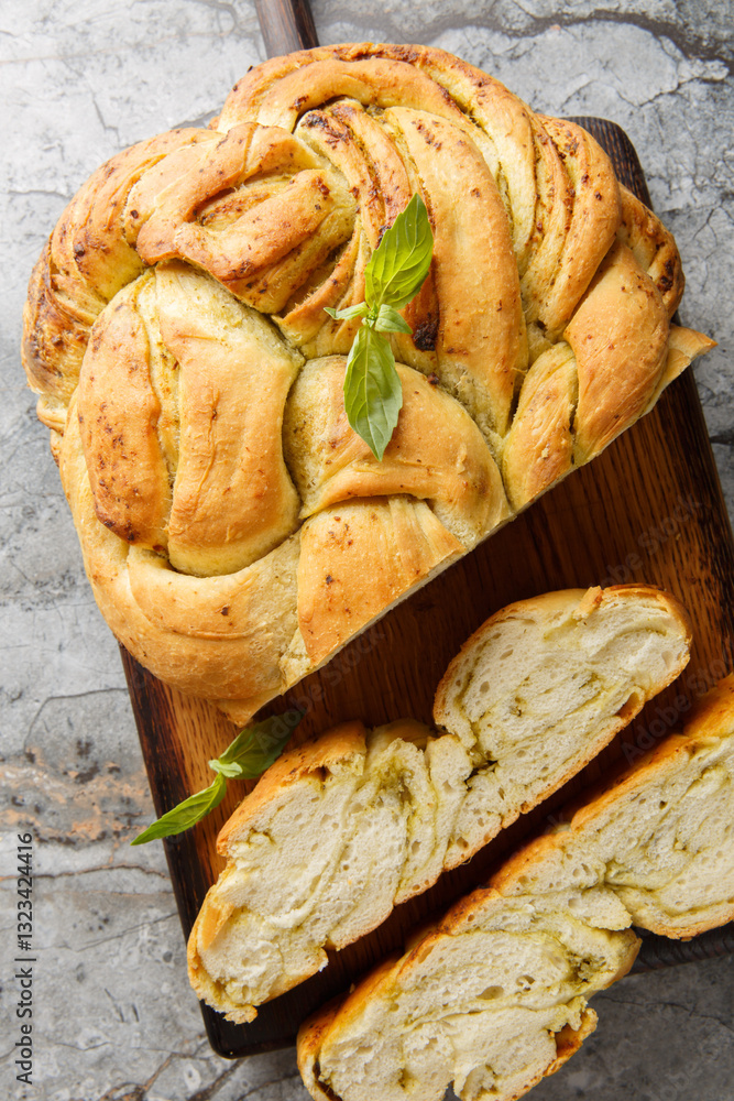 Mediterranean spicy basil pesto braided bread close-up on wooden board on table. Vertical top view from above