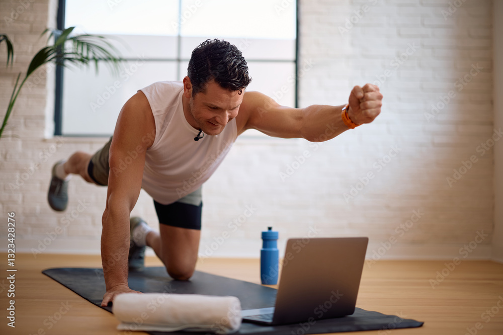 Fototapeta premium Happy athlete working out while watching exercise tutorial on laptop.