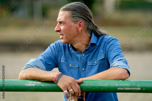 Man with long hair leaning on a green rail in a relaxed outdoor setting. Brandenburg, Germany photo