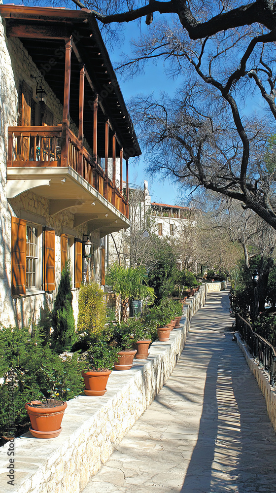 Fototapeta premium Scenic Walkway Lined With Potted Plants Leading to Charming Stone Buildings in Bright Daylight