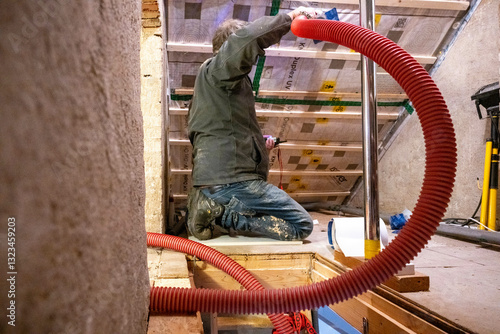 Person kneeling while ingesting insulation in an attic space. Netherlands