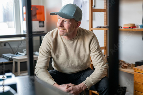 Smiling man in a blue cap sitting in a modern workshop with shelves and equipment. Nijmegen, Netherlands photo